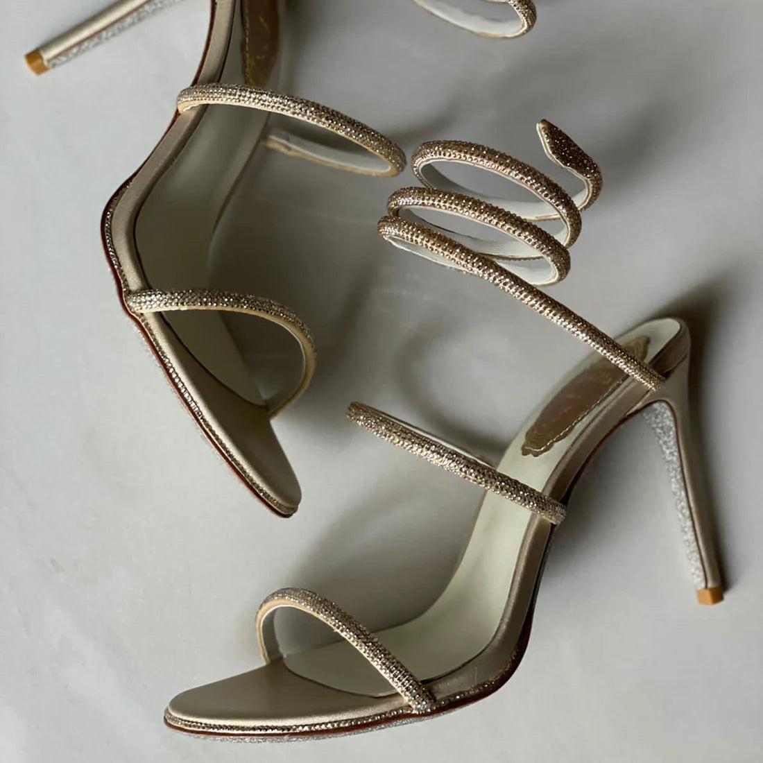 Gold high-heeled shoes with intricate designs on a light gray background