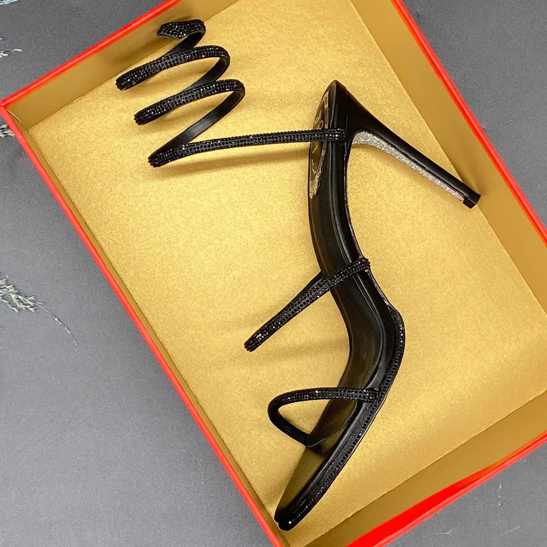 Black high-heeled shoes in a box on a gray surface