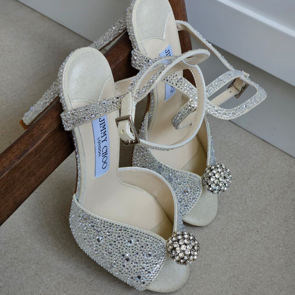 White high-heeled shoes with silver embellishments on a carpeted floor.