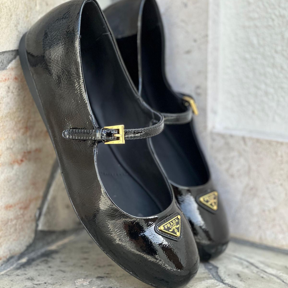 Black patent leather shoes with gold buckles on a textured surface