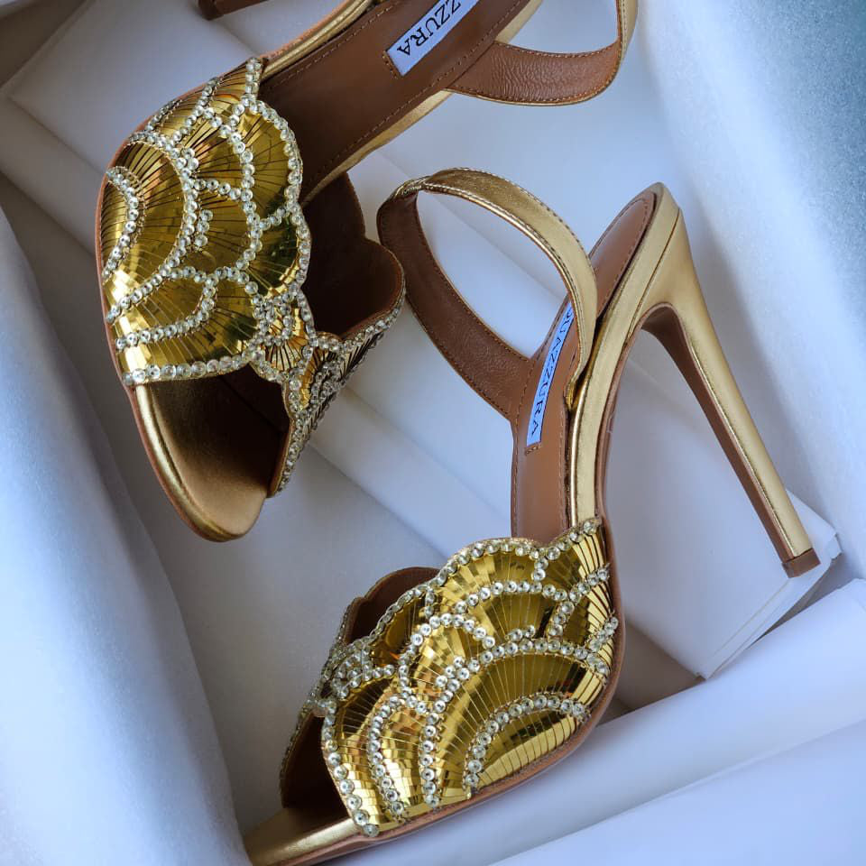 Gold high-heeled shoes with intricate designs on a white background