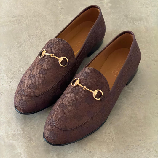 Pair of brown loafers with gold accents on a light gray background