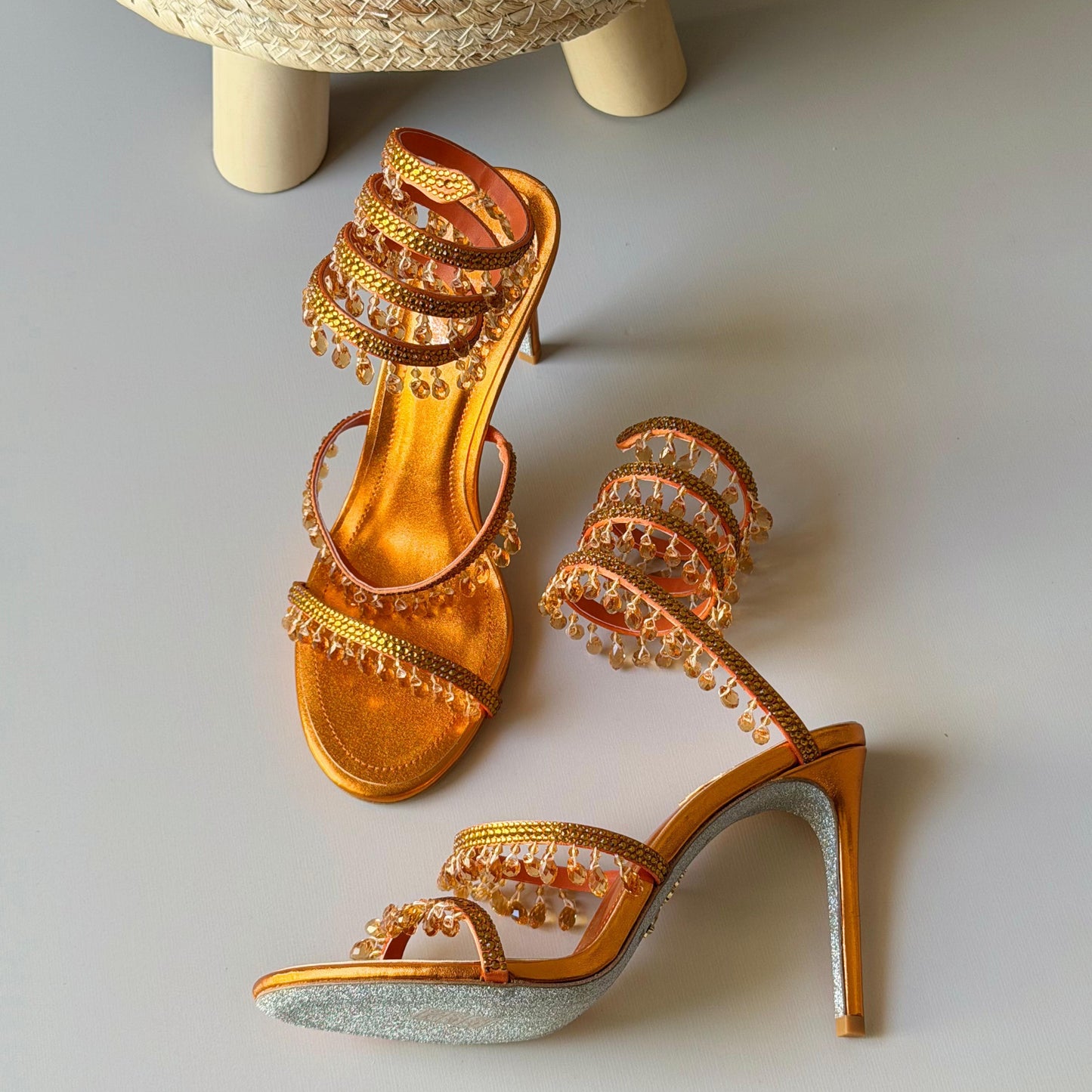 Gold high-heeled shoes with intricate designs on a light gray background