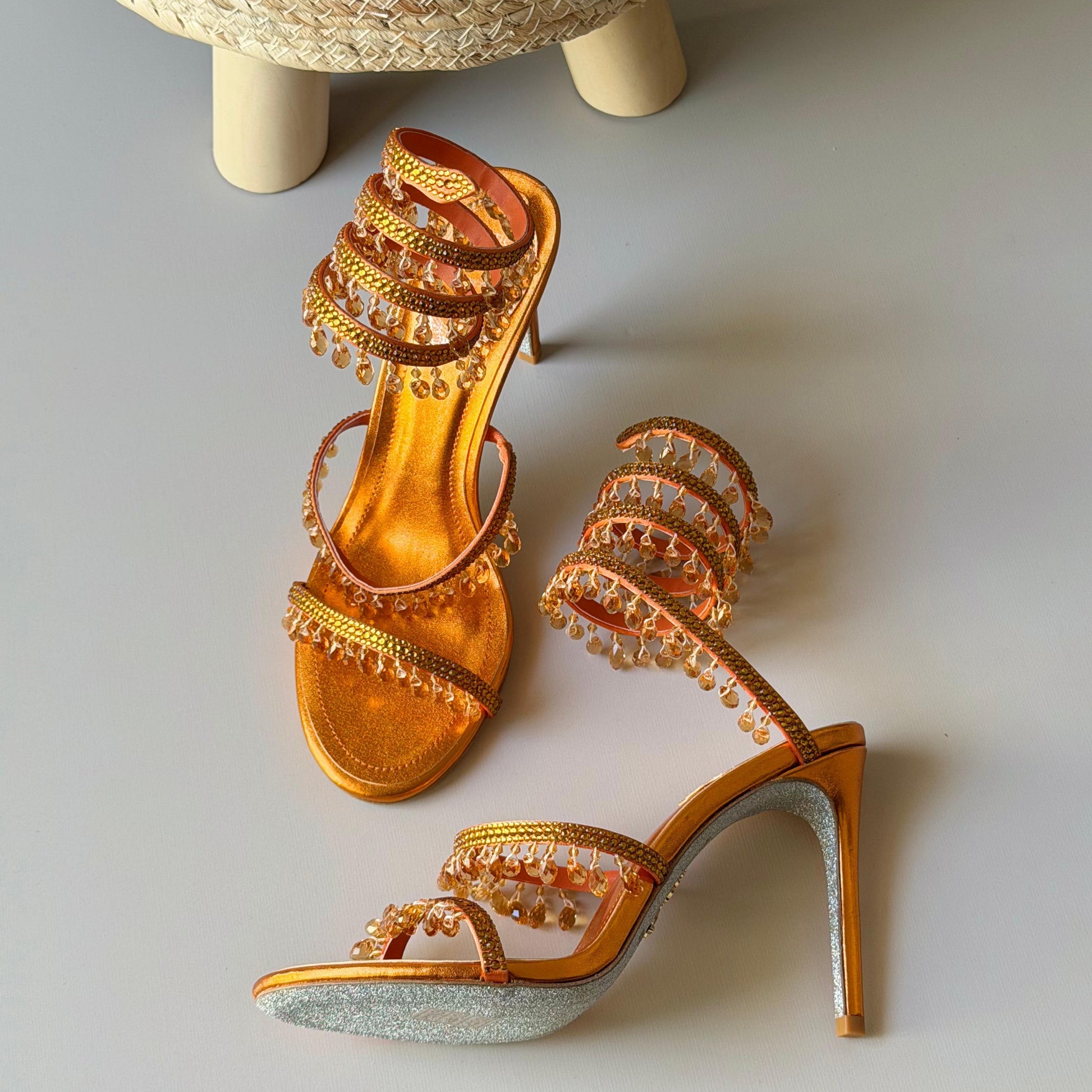 Gold high-heeled shoes with intricate designs on a light gray background