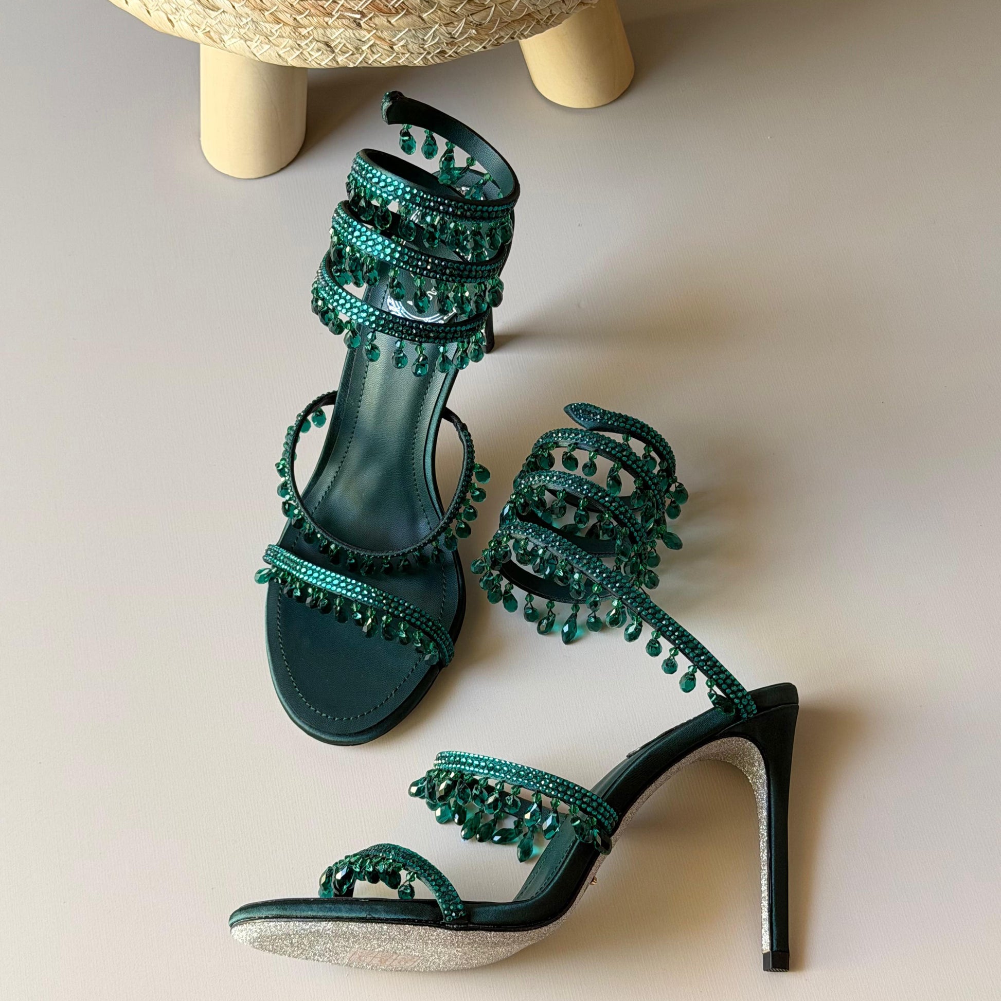 Green high-heeled shoes with embellishments on a neutral background
