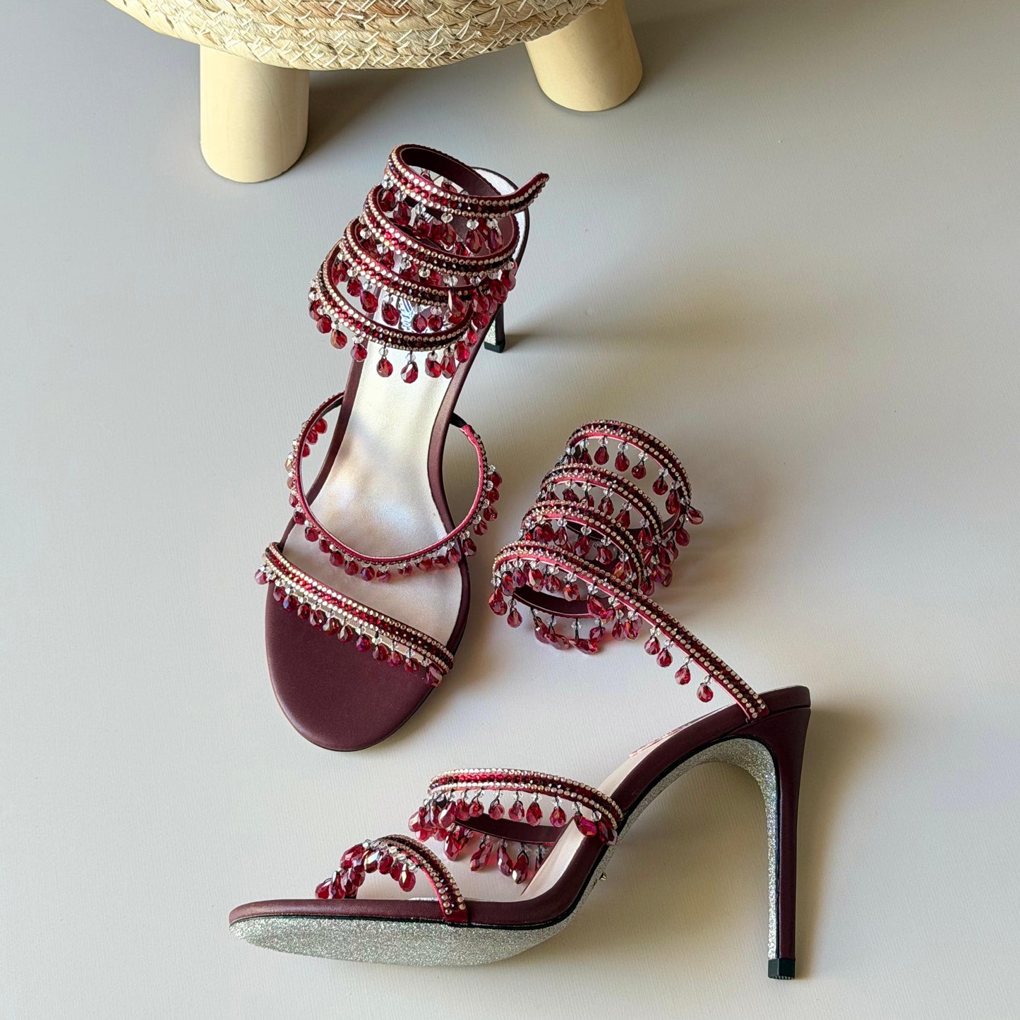 Red high-heeled shoes with decorative elements on a light gray surface.