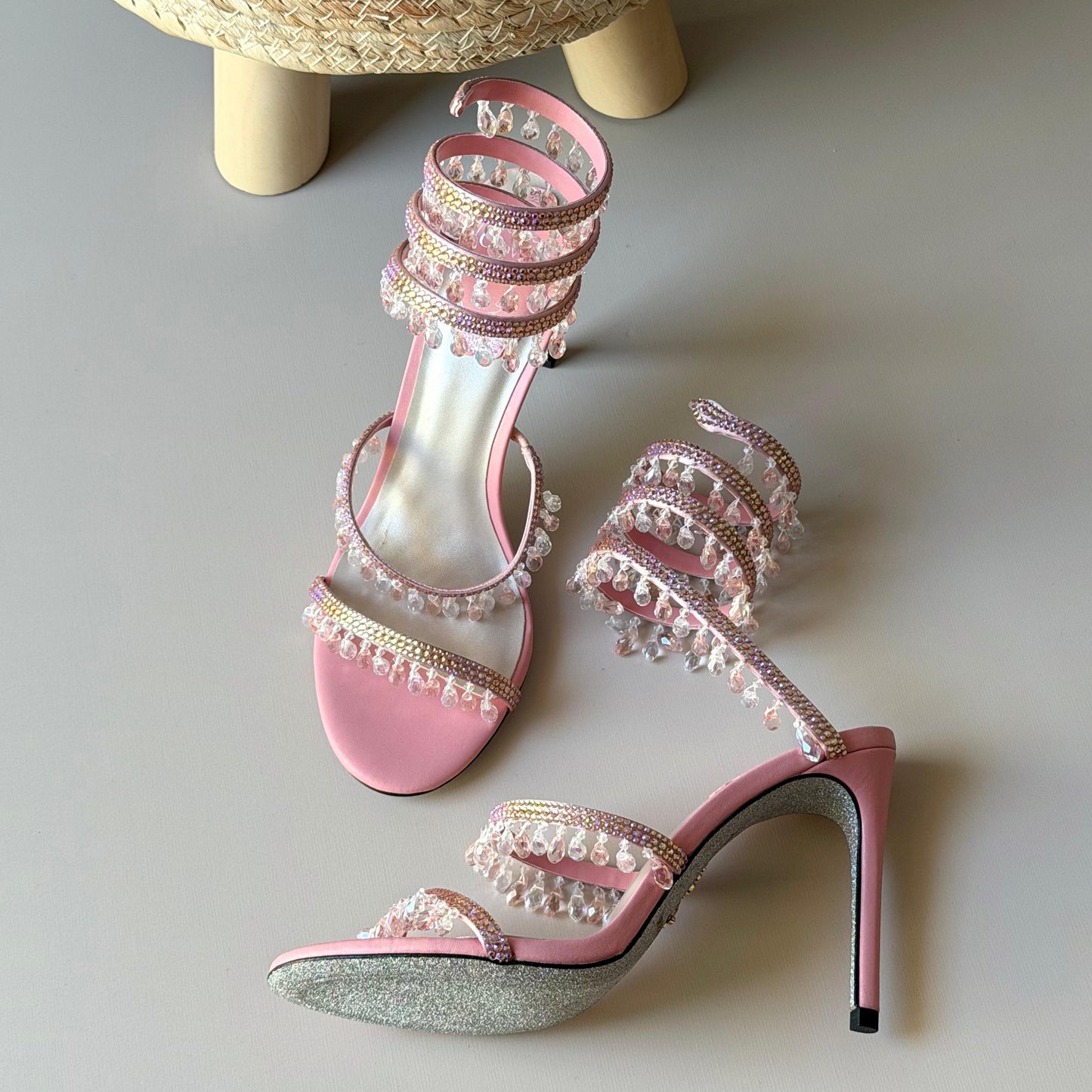 Pink high-heeled sandals with pearl embellishments on a light gray surface.