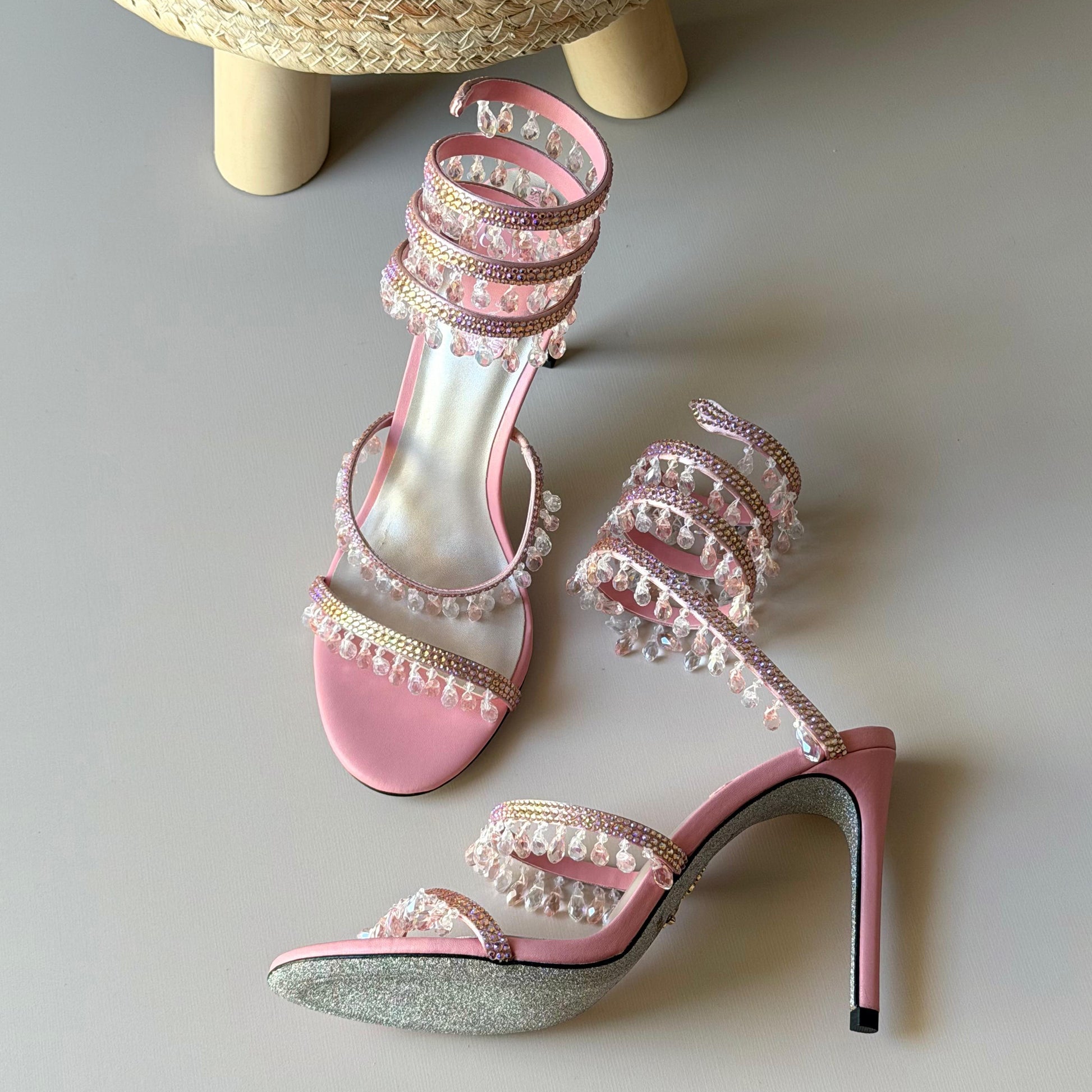 Pink high-heeled sandals with pearl embellishments on a light gray surface.