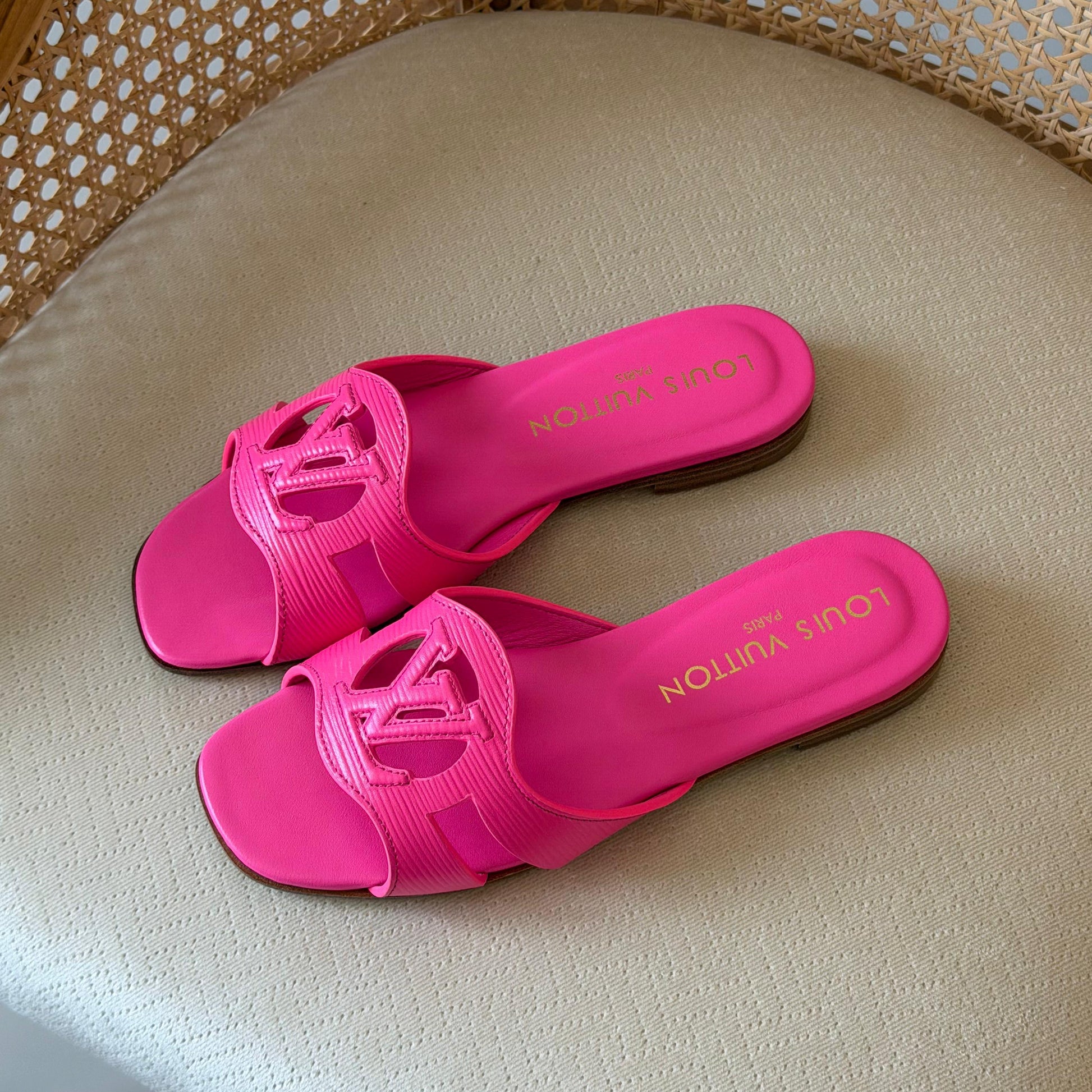 Pair of pink slides on a beige surface with a woven chair background