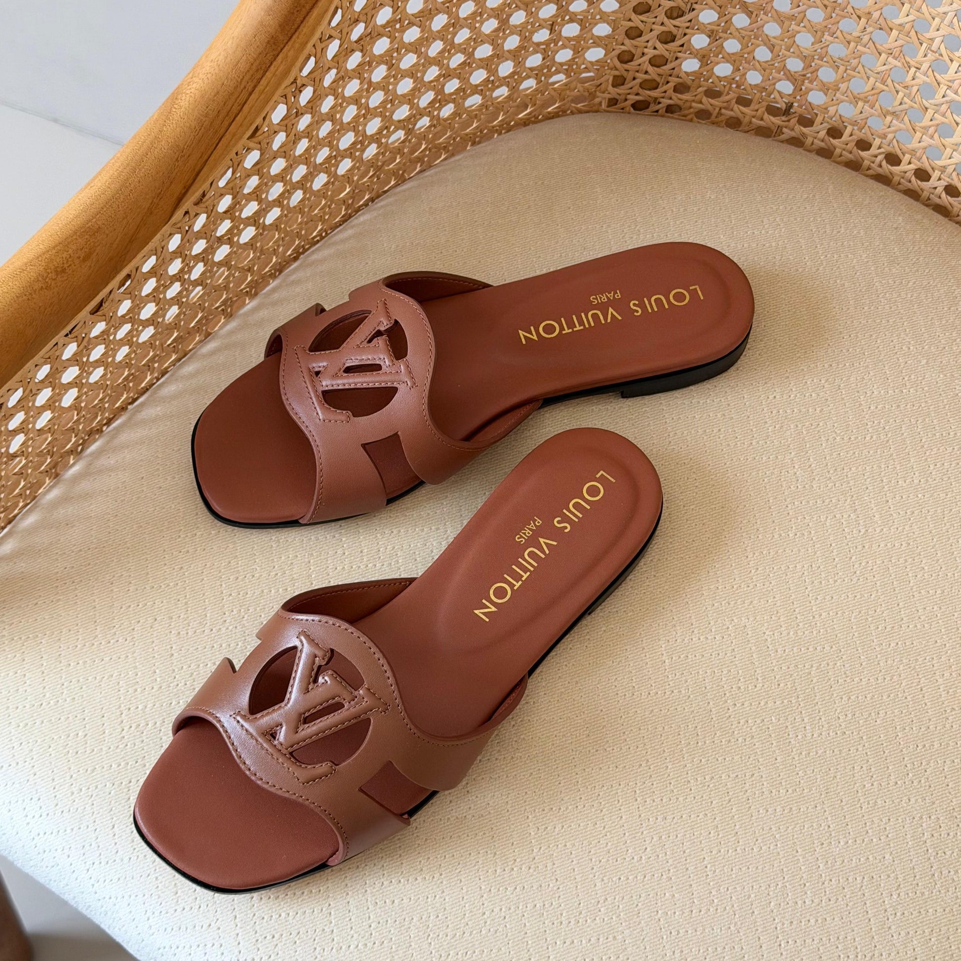 Brown Louis Vuitton sandals on a beige cushion with a wicker chair background