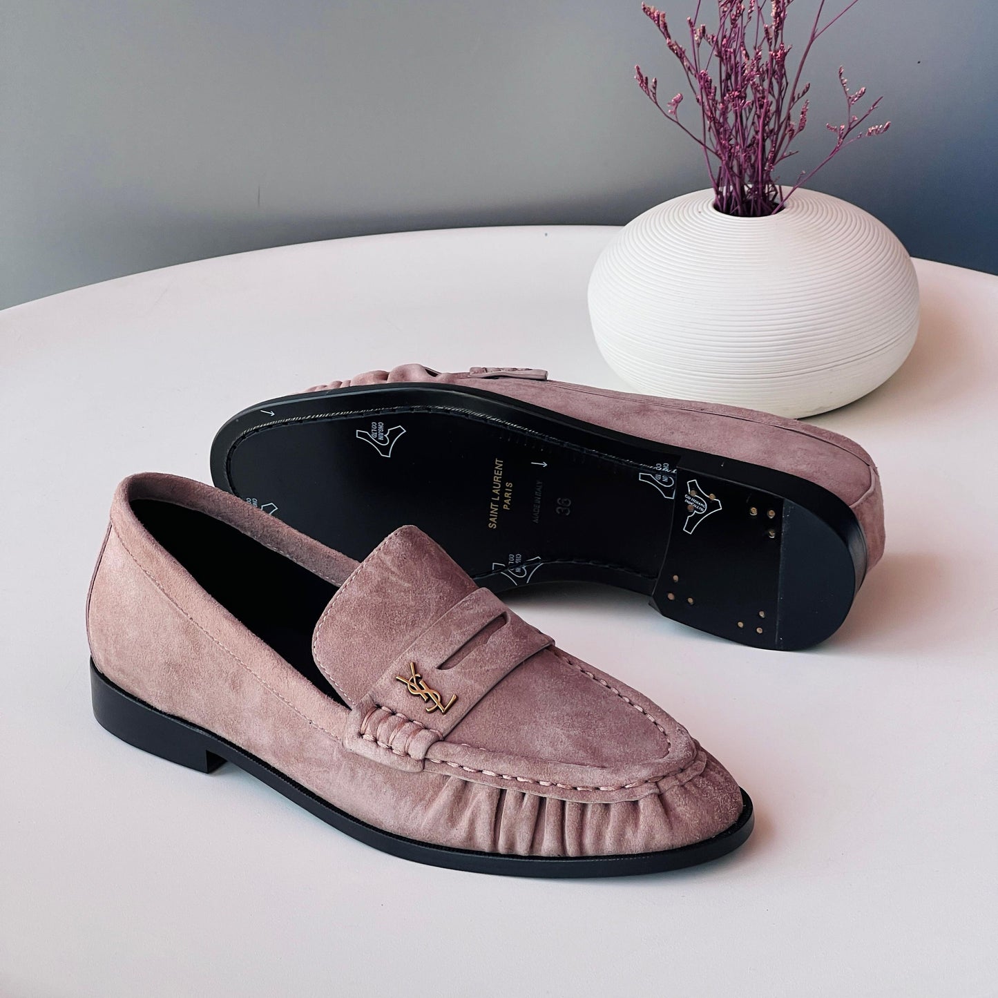 Pair of pink loafers on a white surface with a decorative vase in the background.