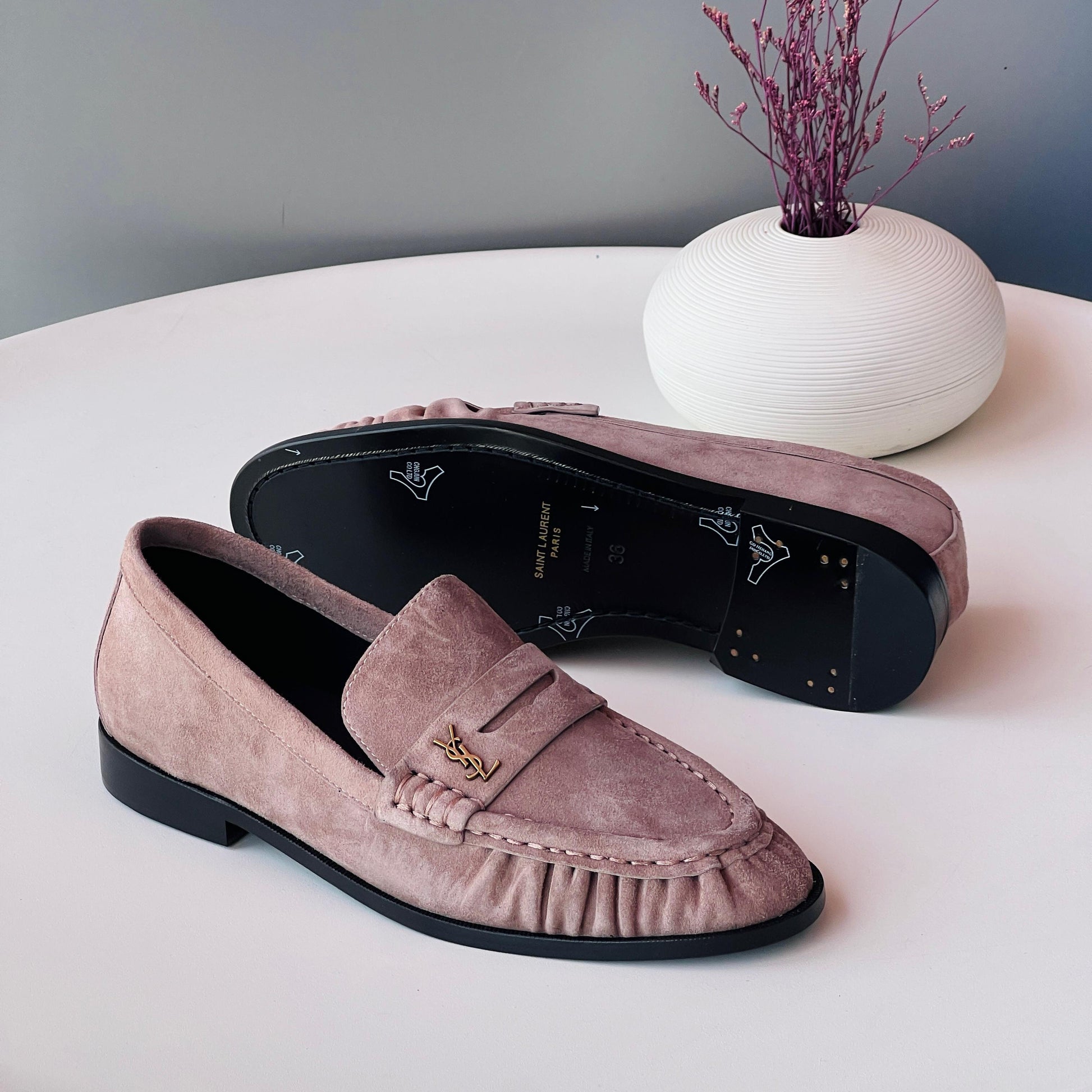 Pair of pink loafers on a white surface with a decorative vase in the background.