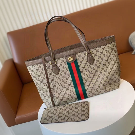 Gucci GG Supreme canvas tote bag with brown leather handles and trim, featuring the signature green and red web stripe and gold interlocking G logo, shown with a matching pouch on a white table against a brown leather background.