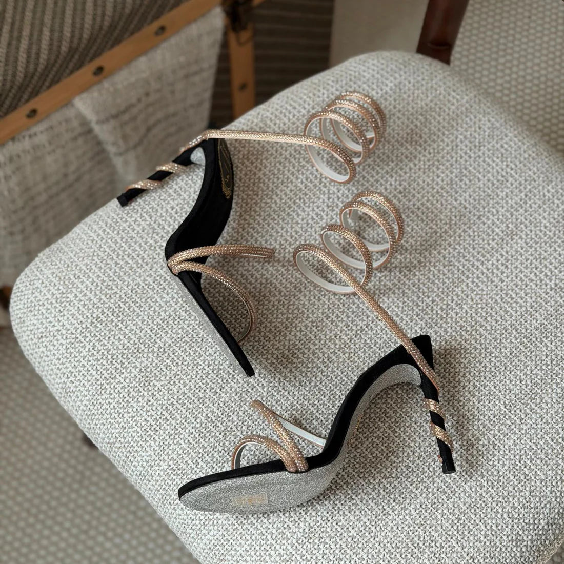 Black high-heeled shoes with gold straps on a textured chair