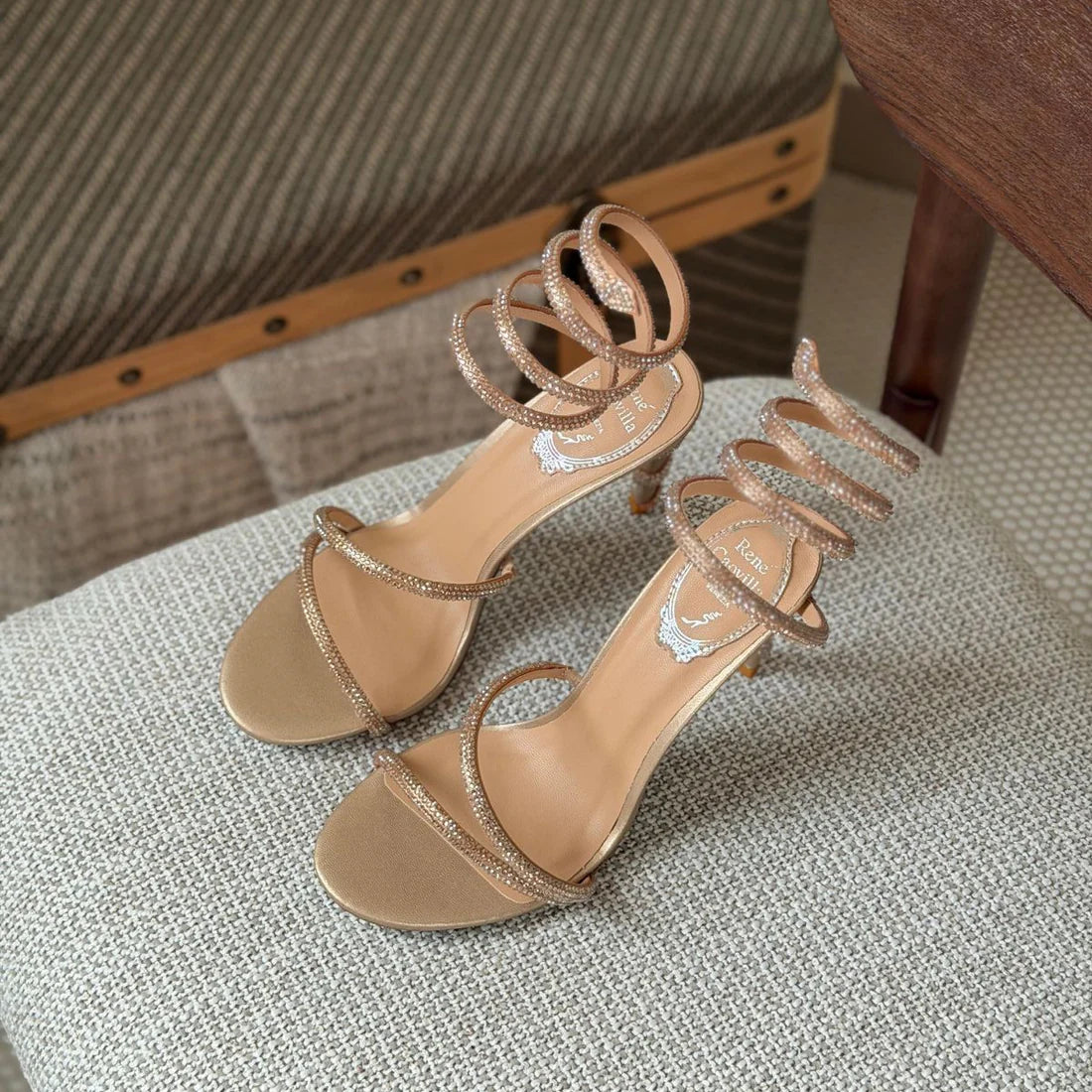 Beige high-heeled sandals with thin straps on a textured surface.