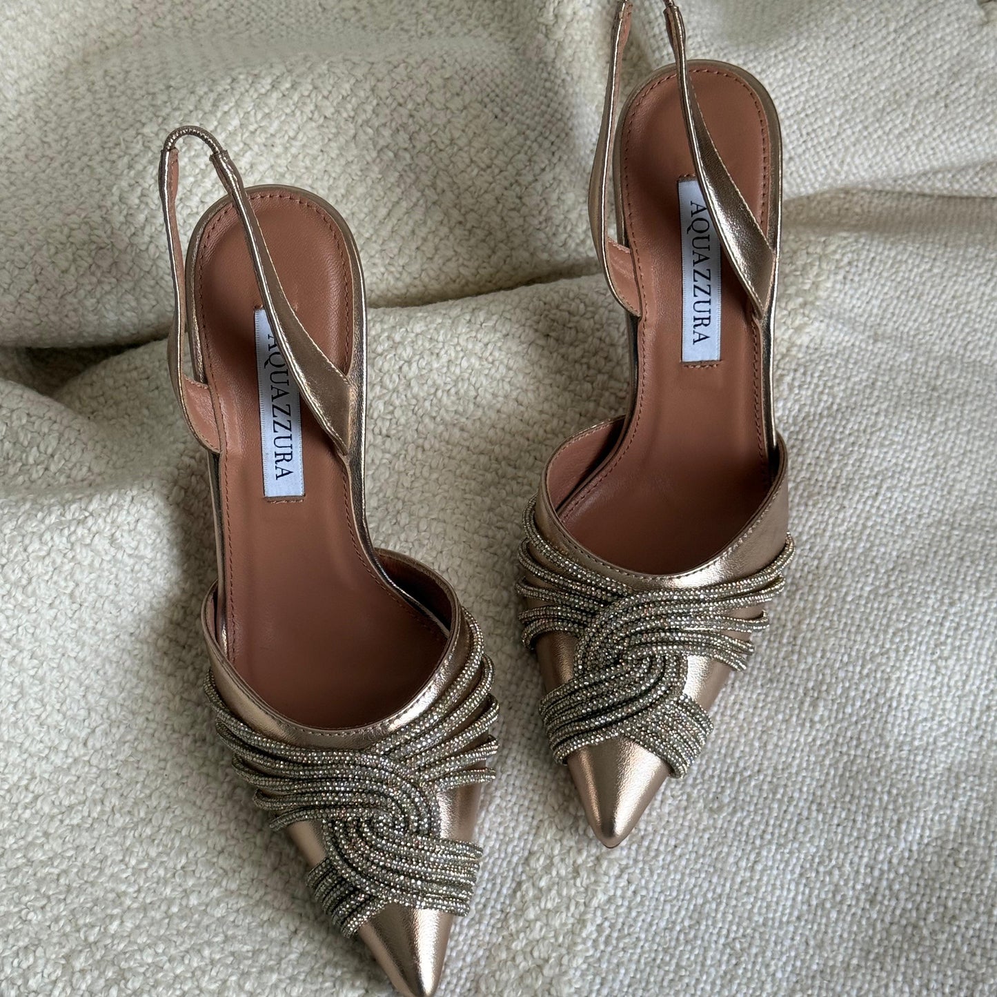 Pair of gold high-heeled shoes with intricate detailing on a textured fabric background